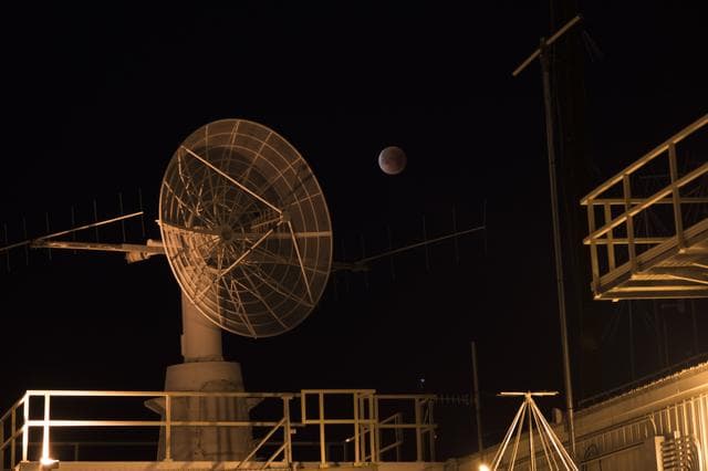 NASA image: NASA Armstrong Flight Research Center’s communications facility with radar dish and antennas is shown having the eclipsed moon overhead during Jan. 31 Super Blue Blood Moon.