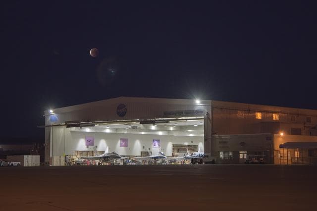 NASA image: Image is NASA Armstrong Flight Research Center's aircraft hangar that houses the jets and other aircraft with the eclipsed moon overhead during Jan. 31 Super Blue Blood Moon.