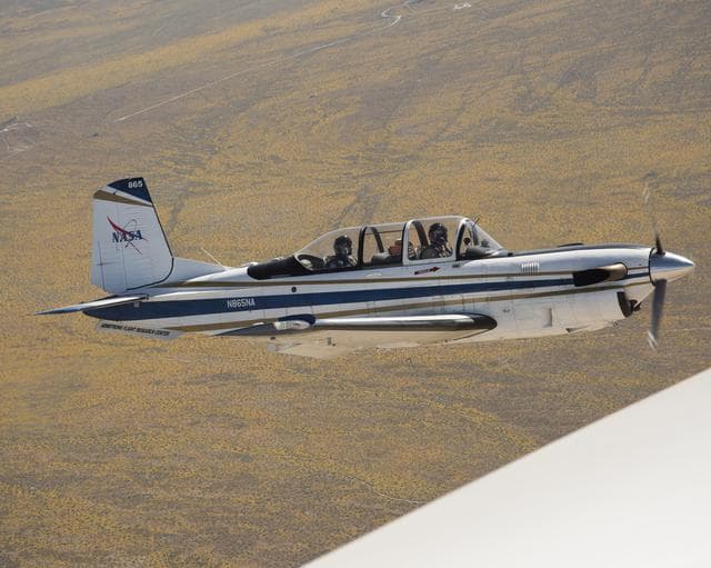 NASA image: NASA Aircraft flies over yellow wildflowers abundant due to rainy winter season. The T-34 aircraft was flown from the agency's Armstrong Flight Research Center.