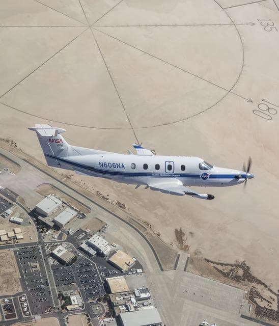 NASA image: NASA Pilatus PC-12 cuts through the desert skies over NASA’s Armstrong Flight Research Center in Edwards, California with the compass rose in the background on Sept. 18, 2024.