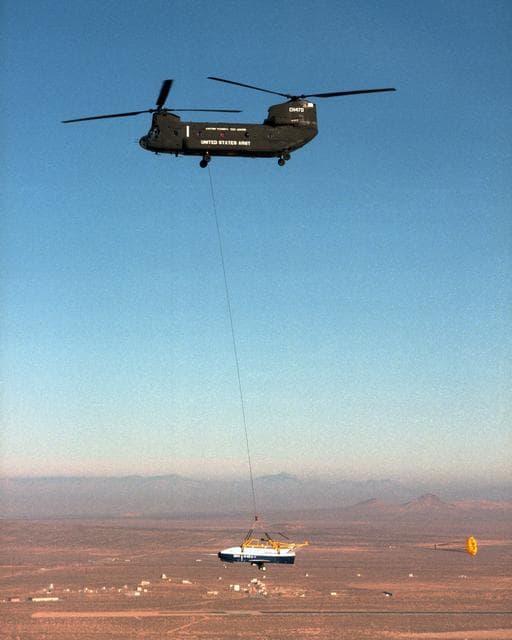 NASA image: With a small stabilization parachute trailing behind, the X-40 sub-scale technology demonstrator is suspended under a U.S. Army CH-47 Chinook cargo helicopter during a captive-carry test flight