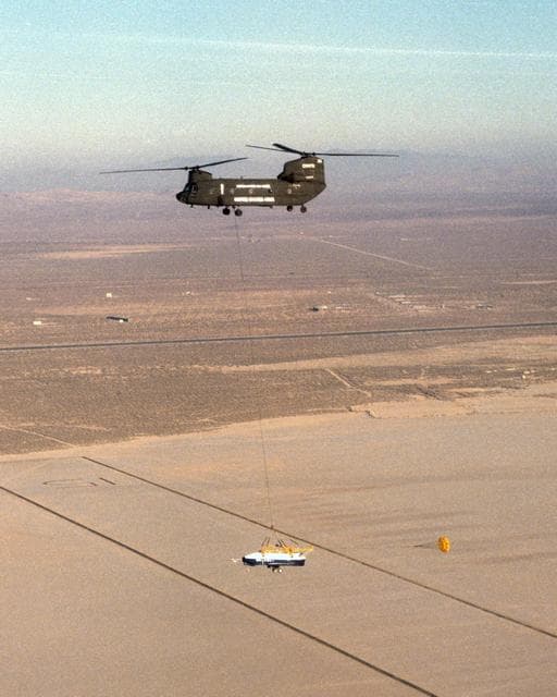 NASA image: The X-40 sub-scale technology demonstrator and its U.S. Army CH-47 Chinook helicopter mothership fly over a dry lakebed runway during a captive-carry test flight at NASA's Dryden Flight Research Center