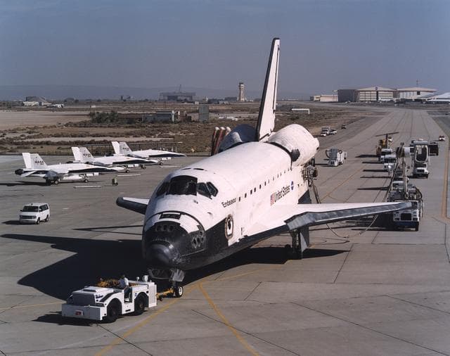 NASA image: The Space Shuttle Endeavour, accompanied by a convoy of recovery vehicles, is towed up the taxiway at NASA's Dryden Flight Research Center at Edwards Air Force Base, California, following its landing on June 19, 2002.  The landing, the 49th to occur at Ed