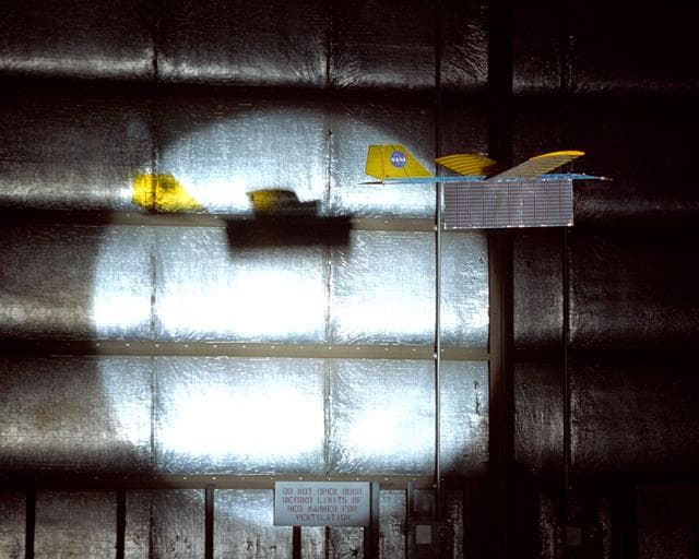 NASA image: An experimental radio-controlled model aircraft casts a unique shadow as it flies inside a Dryden hangar using only a spotlight as an energy source.