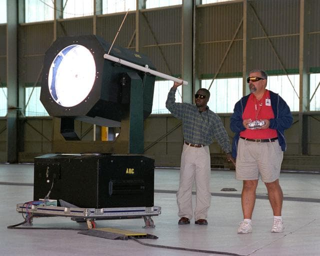NASA image: Dryden Model Shop's Tony Frakowiak remotely flies an experimental model aircraft being powered by a spotlight operated by Dryden aerospace engineer (Code RA) Ryan Warner.