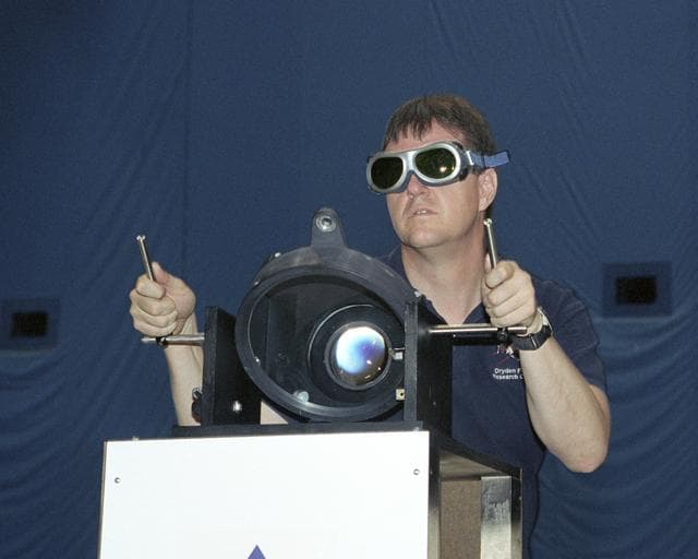 NASA Dryden's Dave Bushman aims the optics of a laser device at a panel on a model aircraft during the first flight demonstration of an aircraft powered by laser light.