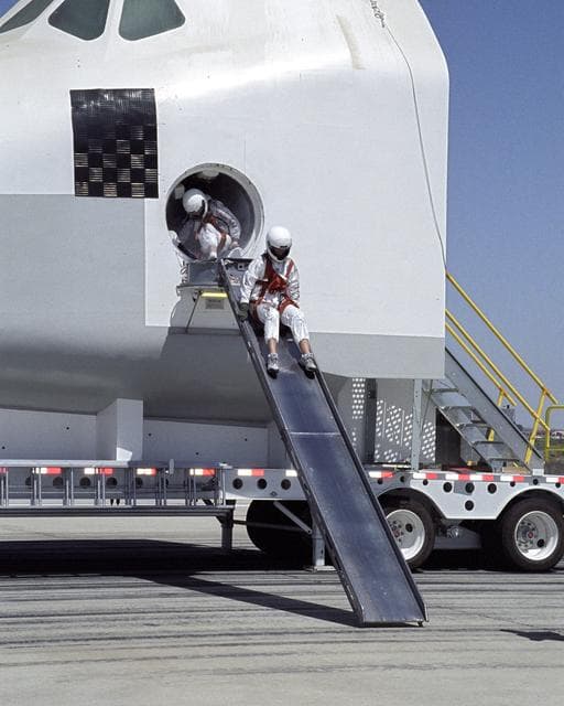 NASA image: A volunteer "astronaut" starts down an exit slide from a Space Shuttle crew compartment mockup during a rescue and recovery training exercise