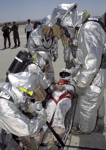 NASA image: Clad in thermal protection suits, fire-rescue crews strap a stand-in "astronaut" into a litter during a Space Shuttle rescue training exercise at Edwards AFB