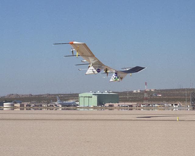 NASA image: The Pathfinder-Plus solar aircraft flies past NASA Dryden's space shuttle hangar and shuttle carrier aircraft as it descends for landing on Rogers Dry Lake.