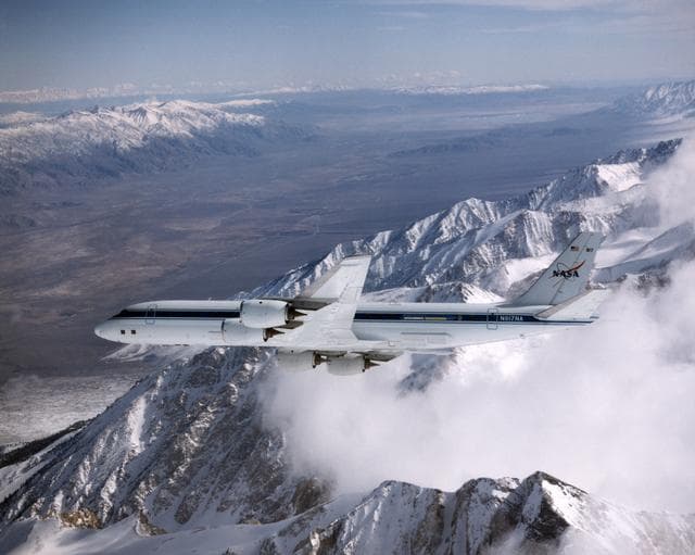 NASA image: DC-8 Airborne Laboratory in banked flight over snow-capped Sierra Nevada mountain range