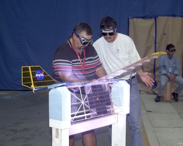 With a laser beam centered on its solar panel, a model aircraft is checked out by technician Tony Frakowiak and researcher Tim Blackwell before its power-beamed demonstration flight.