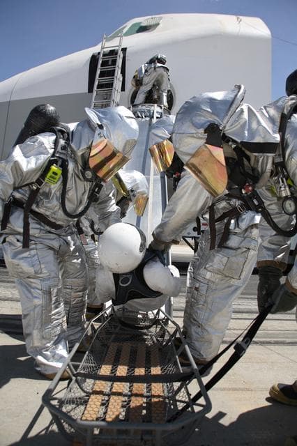 NASA image: Air Force fire/rescue crew place a volunteer "injured astronaut" on a stretcher after exiting the shuttle cabin mockup during the training exercise