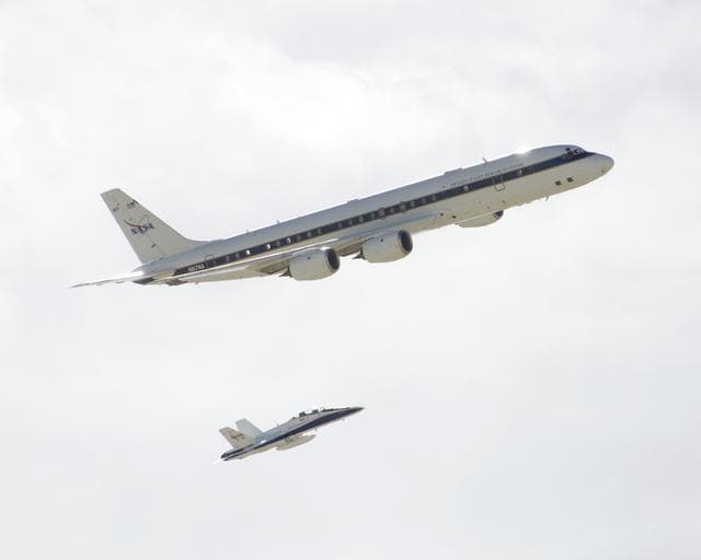 NASA's DC-8 airborne science laboratory is shadowed by a NASA F/A-18 chase plane during a flyover of the Dryden Aircraft Operations Facility in Palmdale, Calif.