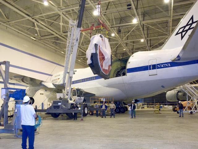NASA image: Technicians with ropes carefully guide the primary mirror assembly as a crane slowly moves it toward its transport cradle after removal from the SOFIA aircraft