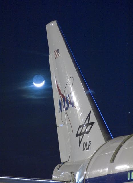 NASA image: Wispy clouds are illuminated by a bright quarter moon behind the tail of NASA's SOFIA flying observatory during telescope characterization testing in 2008