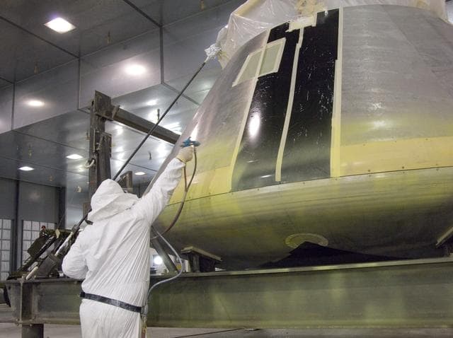 NASA image: A NASA painter applies the first primer coat to NASA's Orion full-scale abort flight test crew module in the Edwards Air Force Base paint hangar.