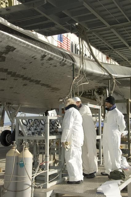 NASA image: Technicians in protective coveralls check pressures of fluid systems during deservicing operations on Space Shuttle Endeavour after its landing at Edwards AFB
