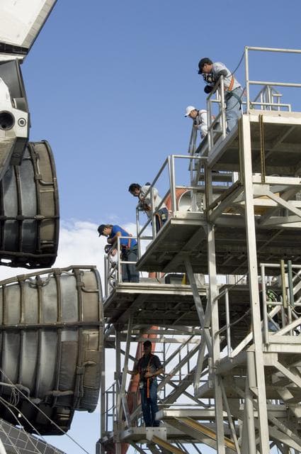NASA image: Technicians monitor the positioning of a workstand as it is moved into place around the main engines of the shuttle Endeavour during deservicing at NASA DFRC