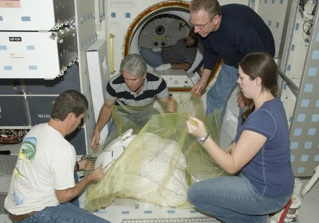 NASA image: United Space Alliance technicians wrap the lower portion of an Extravehicular Mobility Unit (EMU) spacesuit prior to removal from Space Shuttle Endeavour
