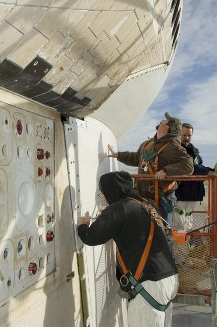 NASA image: Technicians fasten down the flanges of the aerodynamic tail cone after installation on NASA's Space Shuttle Endeavour prior to its ferry flight back to Florida