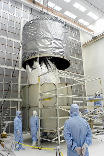 NASA image: KENNEDY SPACE CENTER, FLA. -  Workers in NASA Spacecraft Hangar AE remove a portion of a transportation canister from around the Space Infrared Telescope Facility (SIRTF), which has been returned to the hangar from the launch pad.   SIRTF will remain in the clean room until it returns to the pad in early August. One of NASA's largest infrared telescopes to be launched, SIRTF will obtain images and spectra by detecting the infrared energy, or heat, radiated by objects in space.