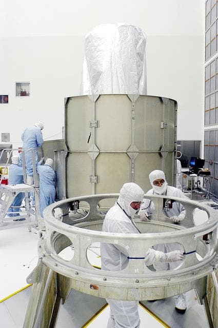 NASA image: KENNEDY SPACE CENTER, FLA. -  Workers in NASA Spacecraft Hangar AE (background) remove sections of the transportation canister from around the Space Infrared Telescope Facility (SIRTF), which has been returned to the hangar from the launch pad.   Additional workers (foreground) prepare the Delta payload attach fitting, from which SIRTF was demated, for further use.  SIRTF will remain in the clean room until it returns to the pad in early August. One of NASA's largest infrared telescopes to be launched, SIRTF will obtain images and spectra by detecting the infrared energy, or heat, radiated by objects in space.