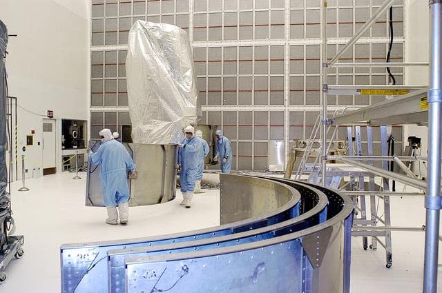 NASA image: KENNEDY SPACE CENTER, FLA. -  Workers in NASA Spacecraft Hangar AE remove sections of the transportation canister from around the Space Infrared Telescope Facility (SIRTF), which has been returned to the hangar from the launch pad.   SIRTF will remain in the clean room until it returns to the pad in early August. One of NASA's largest infrared telescopes to be launched, SIRTF will obtain images and spectra by detecting the infrared energy, or heat, radiated by objects in space.