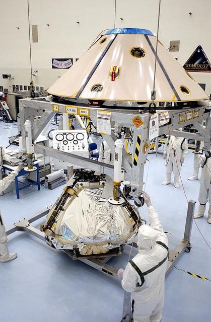 NASA image: KENNEDY SPACE CENTER, FLA. - Workers in the Payload Hazardous Servicing Facility guide the backshell being lowered over the Mars Exploration Rover 1 (MER-1).  The backshell is a protective cover for the rover.  NASA's twin Mars Exploration Rovers are designed to study the history of water on Mars. These robotic geologists are equipped with a robotic arm, a drilling tool, three spectrometers, and four pairs of cameras that allow them to have a human-like, 3D view of the terrain. Each rover could travel as far as 100 meters in one day to act as Mars scientists' eyes and hands, exploring an environment where humans can't yet go.  MER-1 is scheduled to launch June 25 as MER-B aboard a Delta II rocket from Cape Canaveral Air Force Station.