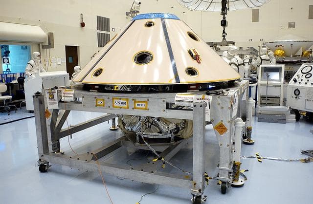 NASA image: KENNEDY SPACE CENTER, FLA. - The backshell is in place over the Mars Exploration Rover 1 (MER-1).  The backshell is a protective cover for the rover.  NASA's twin Mars Exploration Rovers are designed to study the history of water on Mars. These robotic geologists are equipped with a robotic arm, a drilling tool, three spectrometers, and four pairs of cameras that allow them to have a human-like, 3D view of the terrain. Each rover could travel as far as 100 meters in one day to act as Mars scientists' eyes and hands, exploring an environment where humans can't yet go.  MER-1 is scheduled to launch June 25 as MER-B aboard a Delta II rocket from Cape Canaveral Air Force Station.
