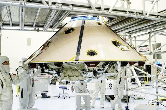 NASA image: KENNEDY SPACE CENTER, FLA. - Workers walk with the suspended backshell/ Mars Exploration Rover 1 (MER-1) as it travels across the floor of the Payload Hazardous Servicing Facility.  The backshell will be attached to the lower heat shield.  NASA's twin Mars Exploration Rovers are designed to study the history of water on Mars. These robotic geologists are equipped with a robotic arm, a drilling tool, three spectrometers, and four pairs of cameras that allow them to have a human-like, 3D view of the terrain. Each rover could travel as far as 100 meters in one day to act as Mars scientists' eyes and hands, exploring an environment where humans can't yet go.  MER-1 is scheduled to launch June 25 as MER-B aboard a Delta II rocket from Cape Canaveral Air Force Station.