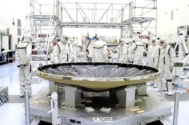 NASA image: KENNEDY SPACE CENTER, FLA. - In the Payload Hazardous Servicing Facility, the heat shield (foreground) is ready to be mated with the upper backshell/ Mars Exploration Rover 1 (MER-1), in the background.  NASA's twin Mars Exploration Rovers are designed to study the history of water on Mars. These robotic geologists are equipped with a robotic arm, a drilling tool, three spectrometers, and four pairs of cameras that allow them to have a human-like, 3D view of the terrain. Each rover could travel as far as 100 meters in one day to act as Mars scientists' eyes and hands, exploring an environment where humans can't yet go.  MER-1 is scheduled to launch June 25 as MER-B aboard a Delta II rocket from Cape Canaveral Air Force Station.