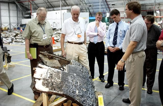 NASA image: KENNEDY SPACE CENTER, FLA. - Adm. Harold Gehman, center, chairman of the Columbia Investigation Accident Board,  looks at a large piece of Columbia debris in the RLV Hangar.  He and other board members are visiting the Hangar as part of the ongoing investigation.  To the right of Gehman are U.S. Representatives Tom Feeney and Dave Weldon.  Recovery efforts as of May 5 included 82,500 pieces of debris weighing 84,800 pounds, almost 40 percent of the total dry weight of the shuttle.  About 25,000 personnel took part, utilizing almost 1.5 million total man-hours in the recovery effort and involving more than 130 federal, state and local agencies.  The operation was also supported by more than 270 organizations that included businesses and volunteer groups.