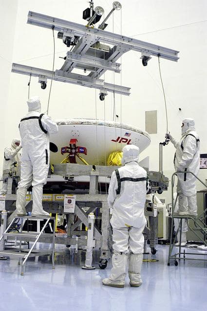 NASA image: KENNEDY SPACE CENTER, FLA. - In the Payload Hazardous Servicing Facility, workers attach a crane to the Mars Exploration Rover-1 (MER-B) as they prepare to lift it onto a spin table during preflight processing of the spacecraft.  The rover is scheduled to launch aboard a Delta II rocket on June 25.  NASA’s twin Mars Exploration Rovers are designed to study the history of water on Mars. These robotic geologists are equipped with a robotic arm, a drilling tool, three spectrometers, and four pairs of cameras that allow them to have a human-like, 3D view of the terrain. Each rover could travel as far as 100 meters in one day to act as Mars scientists' eyes and hands, exploring an environment where humans are not yet able to go. The launch of MER-2 (MER-A) is tentatively set for June 8.
