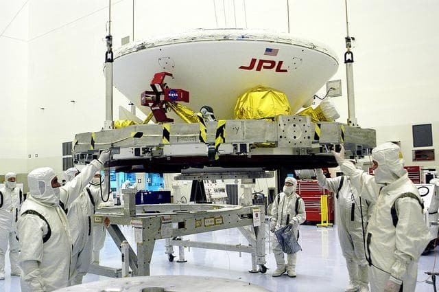 NASA image: KENNEDY SPACE CENTER, FLA. - In the Payload Hazardous Servicing Facility, workers attach a crane to the Mars Exploration Rover-1 (MER-B) as they prepare to lift it onto a spin table during preflight processing of the spacecraft.  The rover is scheduled to launch aboard a Delta II rocket on June 25.  NASA’s twin Mars Exploration Rovers are designed to study the history of water on Mars. These robotic geologists are equipped with a robotic arm, a drilling tool, three spectrometers, and four pairs of cameras that allow them to have a human-like, 3D view of the terrain. Each rover could travel as far as 100 meters in one day to act as Mars scientists' eyes and hands, exploring an environment where humans are not yet able to go. The launch of MER-2 (MER-A) is tentatively set for June 8.