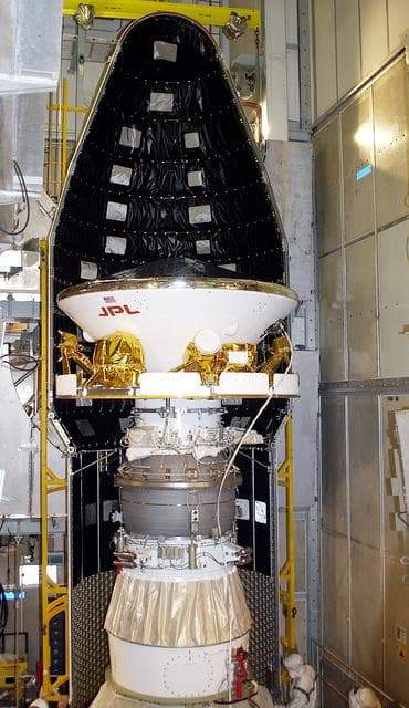 NASA image: KENNEDY SPACE CENTER, FLA. - At Launch Complex 17-A, Cape Canaveral Air Force Station, the first half of the fairing for the Mars Exploration Rover 2 (MER-2) is seen behind the spacecraft.  MER-2 is one of NASA's twin Mars Exploration Rovers designed to study the history of water on Mars. These robotic geologists are equipped with a robotic arm, a drilling tool, three spectrometers, and four pairs of cameras that allow them to have a human-like, 3D view of the terrain. Each rover could travel as far as 100 meters in one day to act as Mars scientists' eyes and hands, exploring an environment where humans can't yet go.  MER-2 is scheduled to launch no earlier than June 8 as MER-A, with two launch opportunities each day during the launch period that closes on June 19.