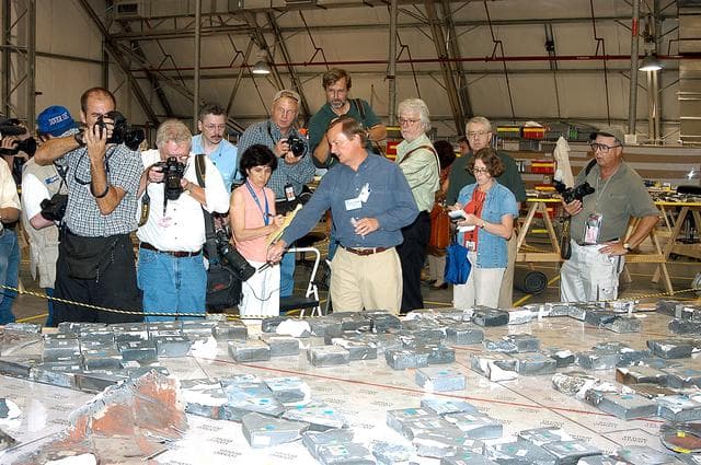 NASA image: KENNEDY SPACE CENTER, FLA. -  In the Columbia Debris Hangar,  Shuttle Launch Director Mike Leinbach  points to some of the tiles recovered from the orbiter as he explains to the media about activities that have taken place since the Columbia accident on Feb. 1, 2003.  STS-107 debris recovery and reconstruction operations are winding down.  To date, nearly 84,000 pieces of debris have been recovered and sent to KSC. That represents about 38 percent of the dry weight of Columbia, equaling almost 85,000 pounds.