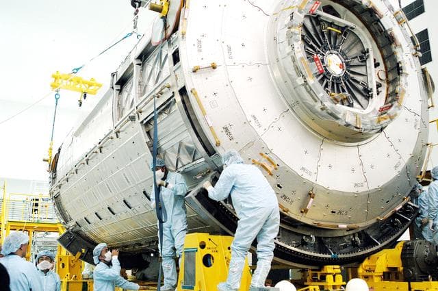 NASA image: KENNEDY SPACE CENTER, FLA. - In the Space Station Processing Facility, workers check the Japanese Experiment Module (JEM) pressure module on its work stand.  A research laboratory, the pressurized module is the first element of the JEM, named "Kibo" (Hope), to be delivered to KSC.   The National Space Development Agency of Japan (NASDA) developed the laboratory at the Tsukuba Space Center near Tokyo and is Japan's primary contribution to the Station. It will enhance the unique research capabilities of the orbiting complex by providing an additional environment for astronauts to conduct science experiments.  The JEM also includes an exposed facility (platform) for space environment experiments, a robotic manipulator system, and two logistics modules. The various JEM components will be  assembled in space over the course of three Shuttle missions.