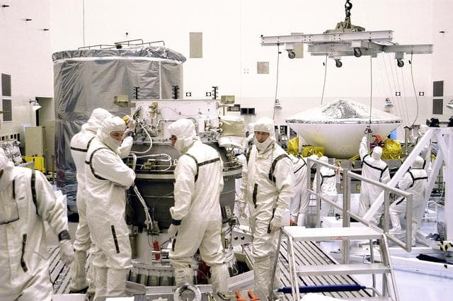 NASA image: KENNEDY SPACE CENTER, FLA. - In the background, right, workers in the Payload Hazardous Servicing Facility get ready to lift Mars Exploration Rover 1 (MER-B) to the third stage of the Delta rocket (foreground) for mating.  The second of twin rovers being sent to Mars, it is equipped with a robotic arm, a drilling tool, three spectrometers, and four pairs of cameras that allow it to have a human-like, 3D view of the terrain. Each rover could travel as far as 100 meters in one day to act as Mars scientists' eyes and hands, exploring an environment where humans can't yet go.  MER-B is scheduled to launch from Launch Pad 17-B, Cape Canaveral Air Force Station, June 26 at one of two available times,  12:27:31 a.m. EDT or 1:08:45 a.m. EDT.