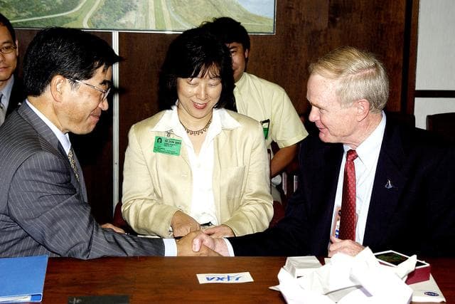 NASA image: KENNEDY SPACE CENTER, FLA. -  Executive Director of NASDA Koji Yamamoto (left) is welcomed to KSC by Center Director Roy Bridges Jr. (right).  On the table between them is the logo of the new Japan Aerospace Exploration Agency, a merger of three Japanese aeronautical and space agencies effective Oct.1, 2003.  Mr. Yamamoto is at KSC for a welcome ceremony involving the arrival of the newest Space Station module, the Japanese Experiment Module/pressurized module.  His visit includes a tour of the Columbia Debris Hangar.