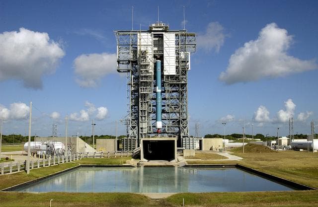 NASA image: KENNEDY SPACE CENTER, FLA. -  On Launch Complex 17-B, Cape Canaveral Air Force Station, the first stage of a Delta II rocket is lifted up the mobile service tower.  Below the rocket is the flame trench, and in the foreground is the overflow pool.  The rocket is being erected to launch the Space InfraRed Telescope Facility (SIRTF).  Consisting of an 0.85-meter telescope and three cryogenically cooled science instruments, SIRTF is one of NASA's largest infrared telescopes to be launched.  SIRTF will obtain images and spectra by detecting the infrared energy, or heat, radiated by objects in space. Most of this infrared radiation is blocked by the Earth's atmosphere and cannot be observed from the ground.