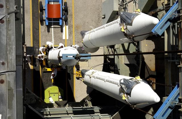 NASA image: KENNEDY SPACE CENTER, FLA. -   This view from the mobile service tower on Launch Complex 17-B, Cape Canaveral Air Force Station, shows two solid rocket boosters (SRBs) already suspended in the tower while another is being lifted.  They are three of nine  46-inch-diameter, stretched SRBs that are being attached to the Delta II Heavy rocket that will launch the Space Infrared Telescope Facility (SIRTF).  Consisting of three cryogenically cooled science instruments and an 0.85-meter telescope, SIRTF is one of NASA's largest infrared telescopes to be launched.  SIRTF will obtain images and spectra by detecting the infrared energy, or heat, radiated by objects in space. Most of this infrared radiation is blocked by the Earth's atmosphere and cannot be observed from the ground.