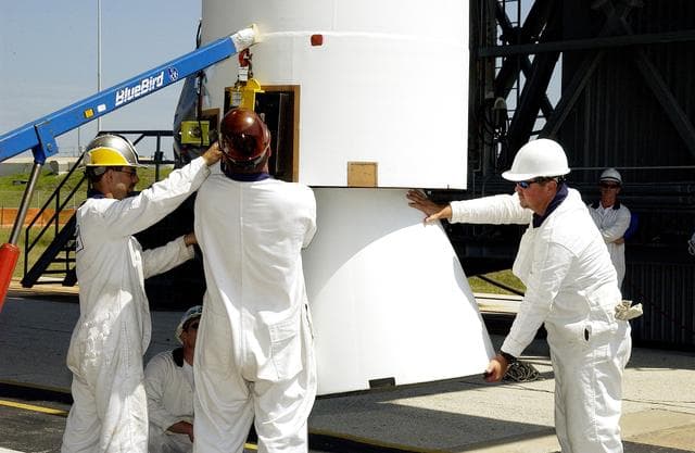 KENNEDY SPACE CENTER, FLA. -   Workers on Launch Complex 17-B, Cape Canaveral Air Force Station, help steady a solid rocket booster (SRB) being lifted into the mobile service tower.  It is one of nine  46-inch-diameter, stretched SRBs that are being attached to the Delta II Heavy rocket that will launch the Space Infrared Telescope Facility (SIRTF).  Consisting of three cryogenically cooled science instruments and an 0.85-meter telescope, SIRTF is one of NASA's largest infrared telescopes to be launched.  SIRTF will obtain images and spectra by detecting the infrared energy, or heat, radiated by objects in space. Most of this infrared radiation is blocked by the Earth's atmosphere and cannot be observed from the ground.