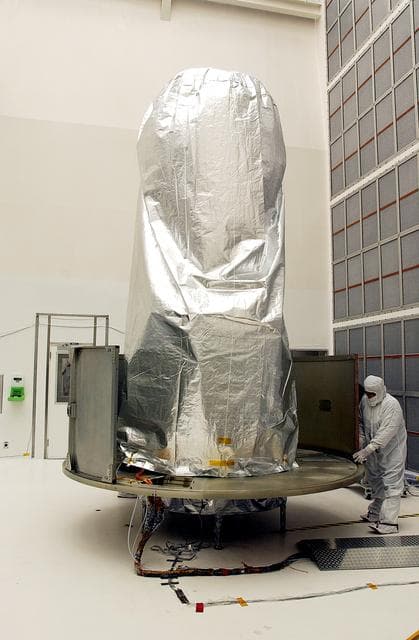 KENNEDY SPACE CENTER, FLA.  -  A worker at Hangar A&E, Cape Canaveral Air Force Station, place the lower panels of the canister around the Space Infrared Telescope Facility (SIRTF).  The spacecraft will be transported to Launch Complex 17-B for mating with its launch vehicle, the Delta II rocket.   SIRTF consists of three cryogenically cooled science instruments and an 0.85-meter telescope, and is one of NASA's largest infrared telescopes to be launched.  SIRTF will obtain images and spectra by detecting the infrared energy, or heat, radiated by objects in space. Most of this infrared radiation is blocked by the Earth's atmosphere and cannot be observed from the ground.