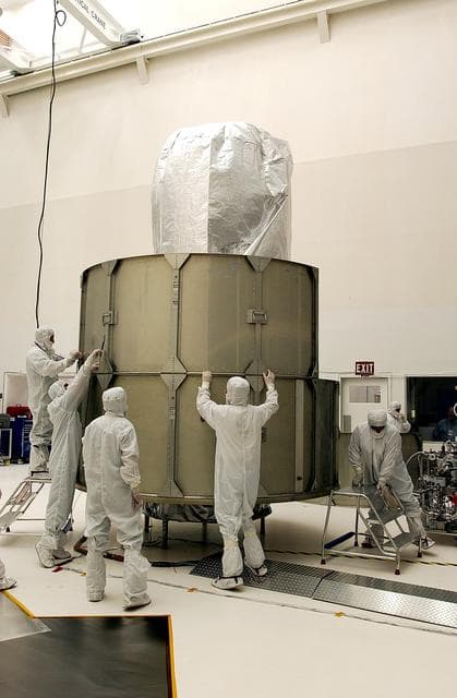 NASA image: KENNEDY SPACE CENTER, FLA.  - Workers at Hangar A&E, Cape Canaveral Air Force Station, place the middle row of panels to encapsulate the Space Infrared Telescope Facility (SIRTF).  The spacecraft will be transported to Launch Complex 17-B for mating with its launch vehicle, the Delta II rocket.   SIRTF consists of three cryogenically cooled science instruments and an 0.85-meter telescope, and is one of NASA's largest infrared telescopes to be launched.  SIRTF will obtain images and spectra by detecting the infrared energy, or heat, radiated by objects in space. Most of this infrared radiation is blocked by the Earth's atmosphere and cannot be observed from the ground.