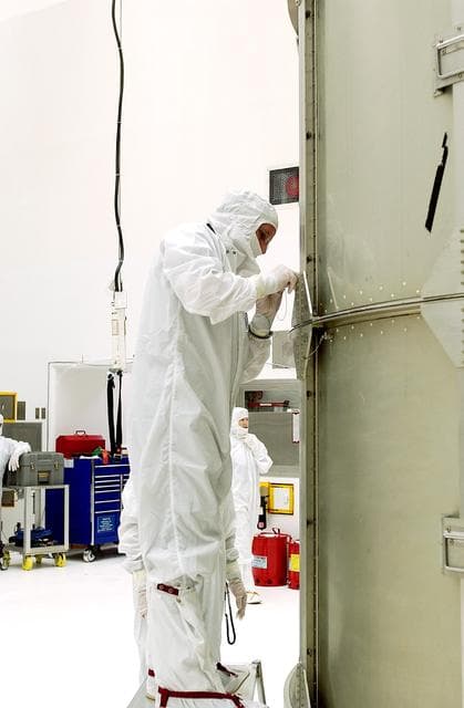 NASA image: KENNEDY SPACE CENTER, FLA.  - A worker at Hangar A&E, Cape Canaveral Air Force Station, tightens the canister around the Space Infrared Telescope Facility (SIRTF).  The spacecraft will be transported to Launch Complex 17-B for mating with its launch vehicle, the Delta II rocket.   SIRTF consists of three cryogenically cooled science instruments and an 0.85-meter telescope, and is one of NASA's largest infrared telescopes to be launched.  SIRTF will obtain images and spectra by detecting the infrared energy, or heat, radiated by objects in space. Most of this infrared radiation is blocked by the Earth's atmosphere and cannot be observed from the ground.
