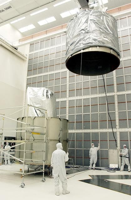 NASA image: KENNEDY SPACE CENTER, FLA.  - Workers at Hangar A&E, Cape Canaveral Air Force Station, help guide the upper canister toward the Space Infrared Telescope Facility (SIRTF) at left.  After encapsulation is complete, the spacecraft will be transported to Launch Complex 17-B for mating with its launch vehicle, the Delta II rocket.   SIRTF consists of three cryogenically cooled science instruments and an 0.85-meter telescope, and is one of NASA's largest infrared telescopes to be launched.  SIRTF will obtain images and spectra by detecting the infrared energy, or heat, radiated by objects in space. Most of this infrared radiation is blocked by the Earth's atmosphere and cannot be observed from the ground.