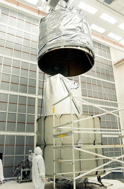 NASA image: KENNEDY SPACE CENTER, FLA.  - Workers at Hangar A&E, Cape Canaveral Air Force Station, lower the upper canister toward the Space Infrared Telescope Facility (SIRTF) below.  After encapsulation is complete, the spacecraft will be transported to Launch Complex 17-B for mating with its launch vehicle, the Delta II rocket.   SIRTF consists of three cryogenically cooled science instruments and an 0.85-meter telescope, and is one of NASA's largest infrared telescopes to be launched.  SIRTF will obtain images and spectra by detecting the infrared energy, or heat, radiated by objects in space. Most of this infrared radiation is blocked by the Earth's atmosphere and cannot be observed from the ground.