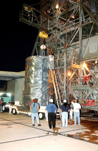 NASA image: KENNEDY SPACE CENTER, FLA.  -  Before dawn, the Space Infrared Telescope Facility (SIRTF) is attached to an overhead crane that will lift it up the mobile service tower on Launch Pad 17-B, Cape Canaveral Air Force Station.  SIRTF will be attached to the Delta II rocket and encapsulated in its fairing before launch.   Consisting of three cryogenically cooled science instruments and an 0.85-meter telescope, SIRTF is one of NASA’s largest infrared telescopes to be launched.  It is the fourth and final element in NASA’s family of orbiting “Great Observatories.”  SIRTF will obtain images and spectra by detecting the infrared energy, or heat, radiated by objects in space. Most of this infrared radiation is blocked by the Earth's atmosphere and cannot be observed from the ground.