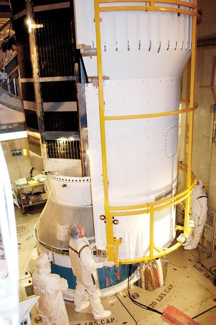 NASA image: KENNEDY SPACE CENTER, FLA.  - In the mobile service tower on Launch Pad 17-B, Cape Canaveral Air Force Station, workers move the first half of the fairing around the Space Infrared Telescope Facility (SIRTF) behind it for encapsulation. SIRTF will obtain images and spectra by detecting the infrared energy, or heat, radiated by objects in space. Consisting of a 0.85-meter telescope and three cryogenically cooled science instruments, SIRTF will be the largest infrared telescope ever launched into space. It is the fourth and final element in NASA’s family of orbiting “Great Observatories.” Its highly sensitive instruments will give a unique view of the Universe and peer into regions of space that are hidden from optical telescopes.