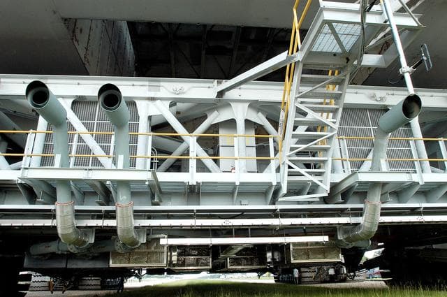 NASA image: KENNEDY SPACE CENTER, FLA.  -  A closeup of crawler-transportation (CT) number 2 shows the new muffler system on the vehicle.  The CT also recently underwent modifications to the cab.   The CT is transporting a Mobile Launch Platform (MLP).  The CT moves Space Shuttle vehicles, situated on the MLP, between the VAB and launch pad.  Moving on four double-tracked crawlers, the CT uses a laser guidance system and a leveling system for the journey that keeps the top of a Space Shuttle vertical within plus- or minus-10 minutes of arc.  The system enables the CT-MLP-Shuttle to negotiate the ramp leading to the launch pads and keep the load level.  Unloaded, the CT weighs 6 million pounds.  Seen on top of the MLP are two tail service masts that support the fluid, gas and electrical requirements of the orbiter’s liquid oxygen and liquid hydrogen aft umbilicals.